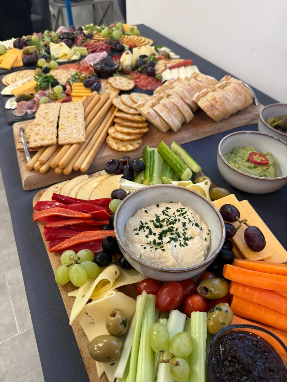 Assorted platter of fruits, vegetables, bread, and dips on a wooden board.