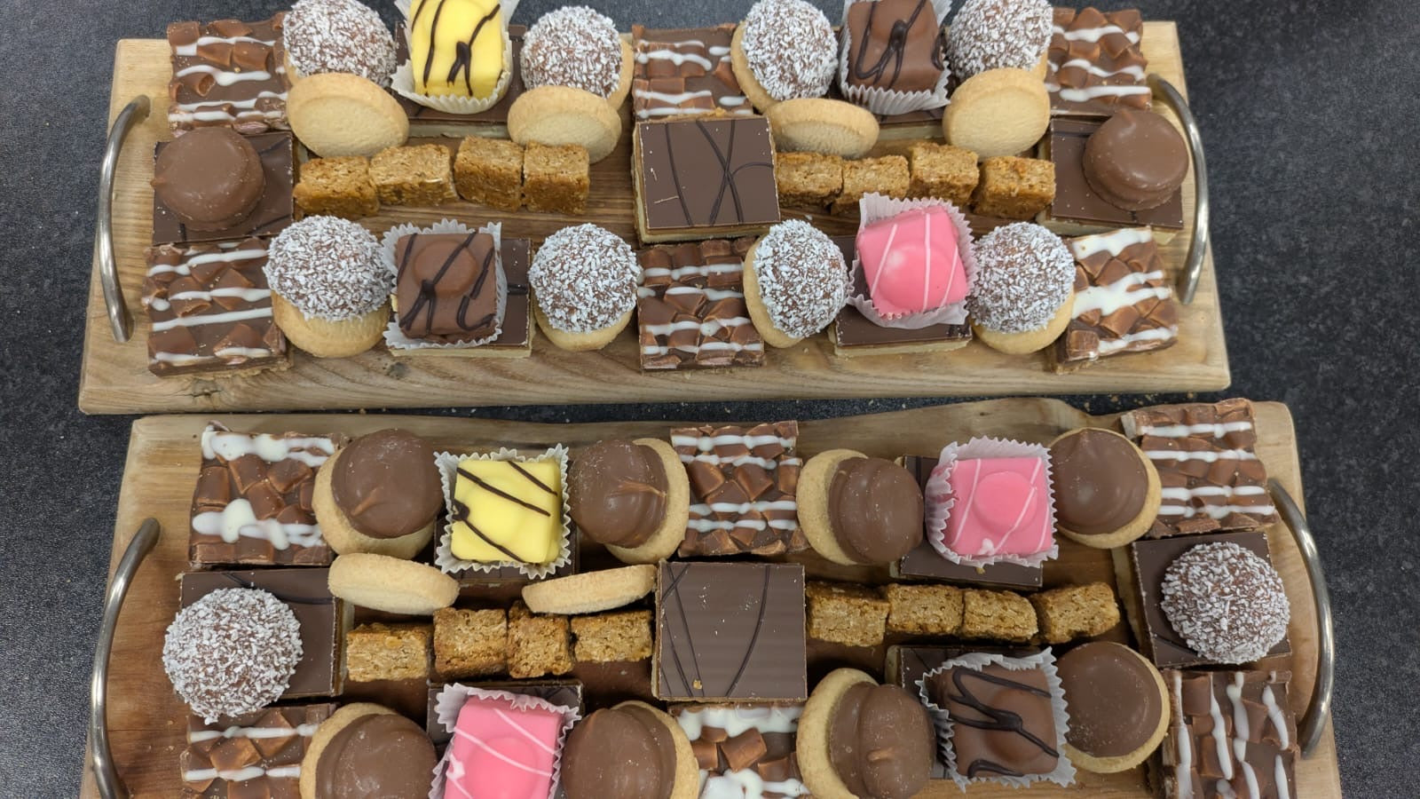Two wooden serving boards filled with assorted chocolates, cookies, and sweets, arranged on a dark countertop.